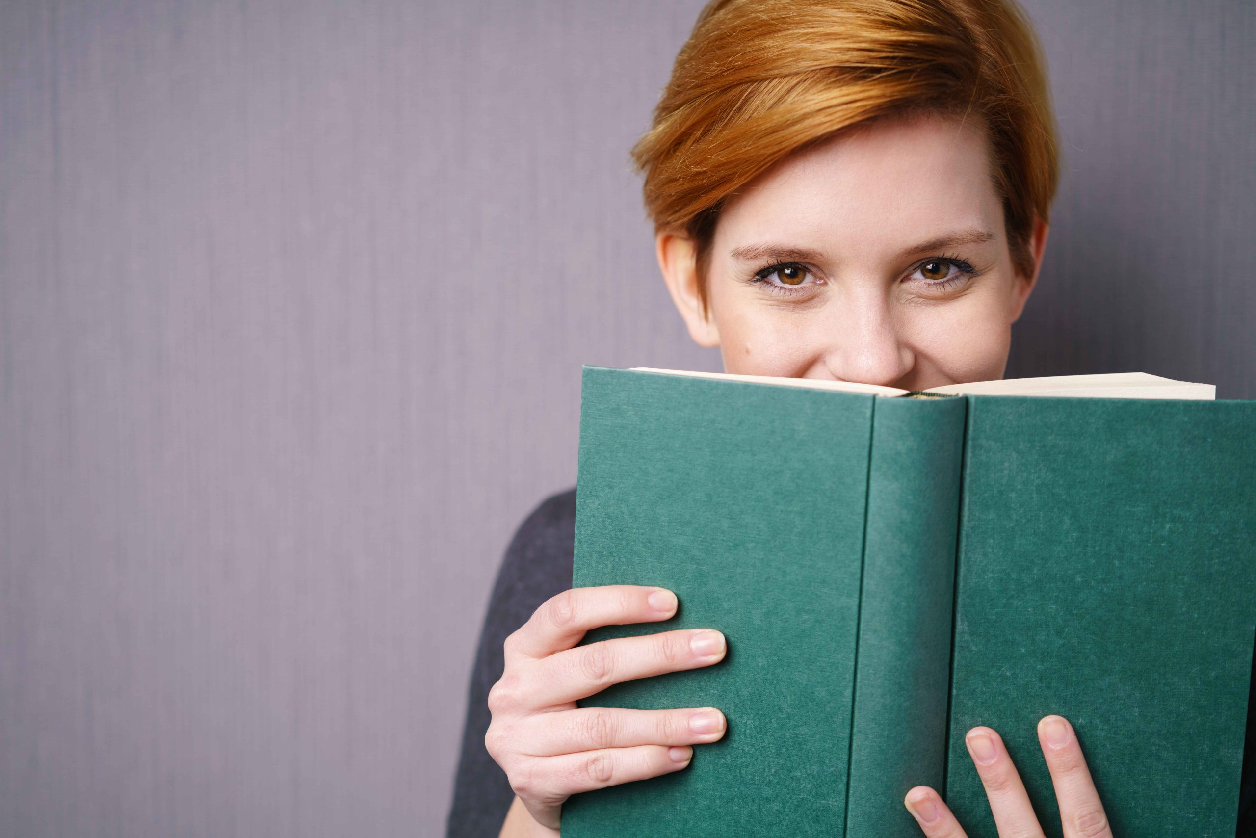 Eine weibliche Person mit einem grünen Buch in der Hand und halb vorm Gesicht