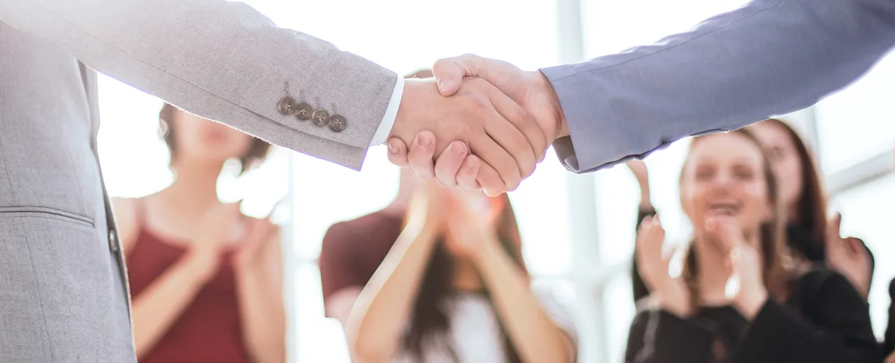 Hanschlag von zwei Personen mit mehreren applaudierenden Personen im Hintergrund